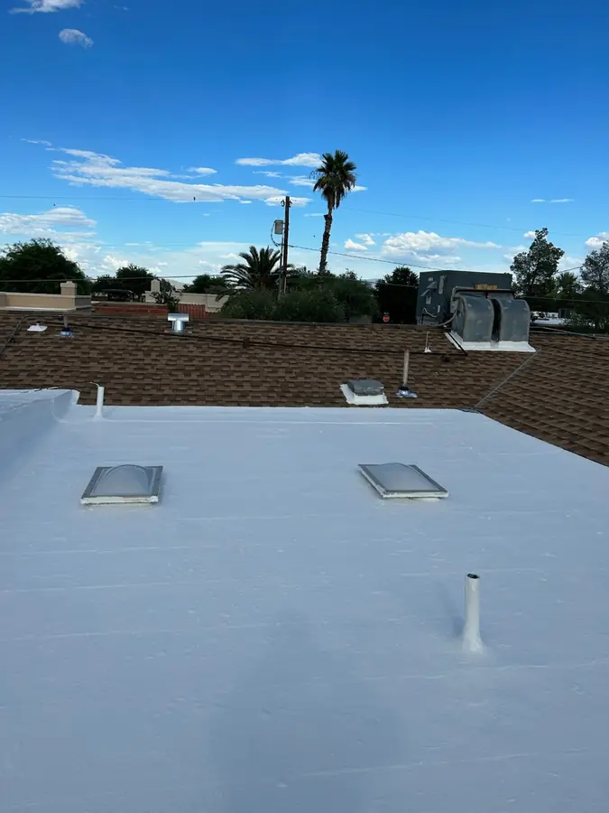 White coated roof with skylights, pipes, vents and adjacent shingle roofing